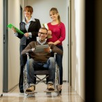 Businessman on a wheelchair with his colleagues in the corridor